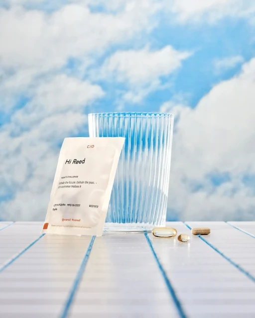 Product shot featuring a C/ID Hi Reed single-dose packet, clear faceted glass, and scattered supplements against a sky backdrop.