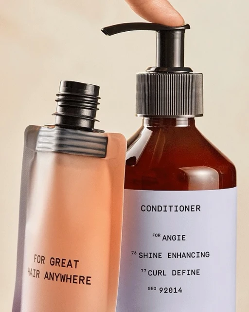 Close-up studio shot of two cosmetic bottles, one clear and one opaque, with black text labels on a beige background. Pumping the product.