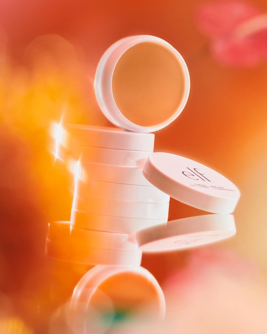 Stacked white cosmetic jars with a blurred, golden-orange background. The composition is softly lit and abstract in its presentation.