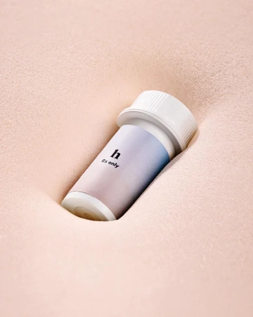 A small white prescription bottle with a blue and white gradient label resting in a soft pink indented foam surface.