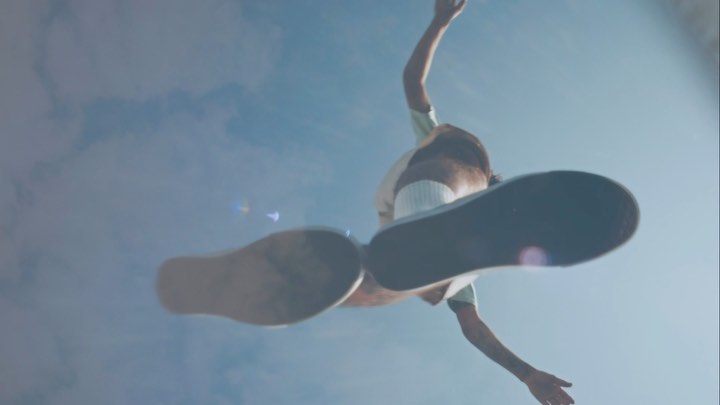 Low-angle shot of person with brown hair wearing sneakers in a sky filled with clouds, looking up from below, motion blur.