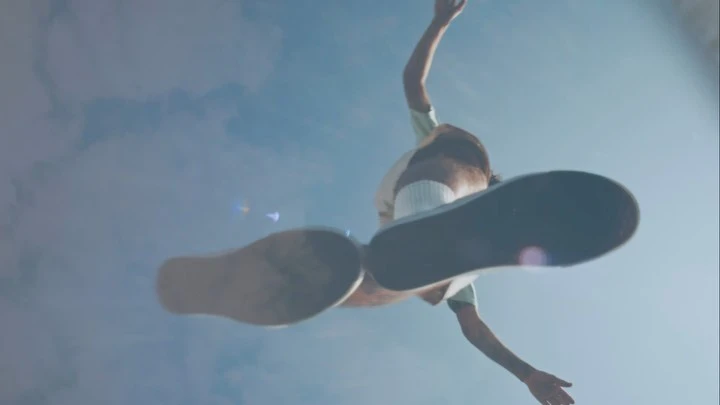 Low-angle shot of person with brown hair wearing sneakers in a sky filled with clouds, looking up from below, motion blur.