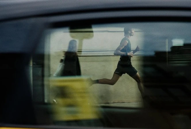 A man in athletic wear is running outside; a car window's reflection shows a blurred figure in the reverse direction.