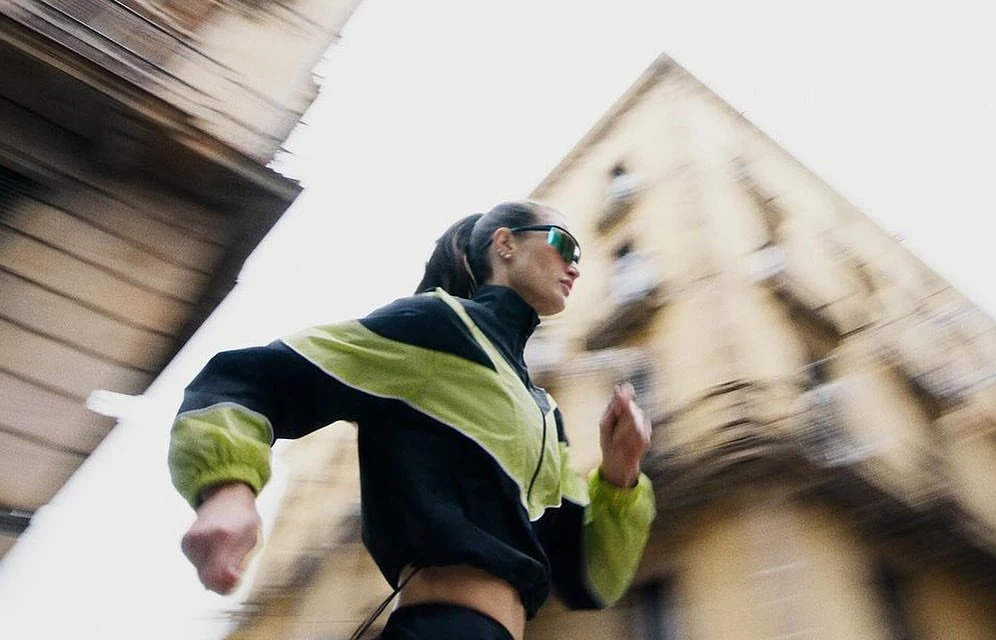 Woman in athletic wear running in an urban setting with blurred motion. Building in the background, low angle, and natural light.