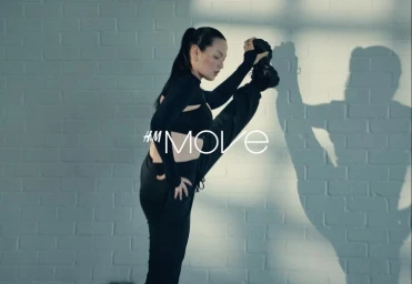 Woman in black athletic crop top and sweatpants stretching her leg against a painted brick wall