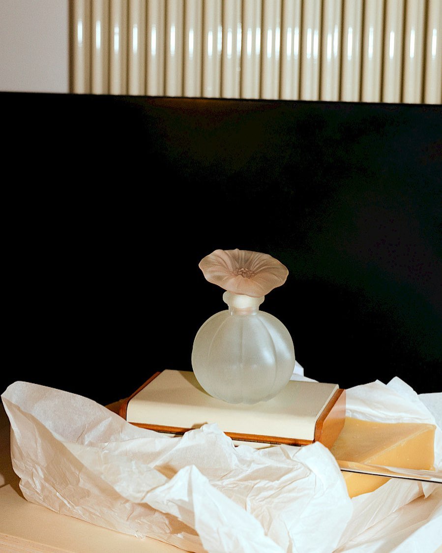 Elegant perfume bottle with a flower-shaped stopper sits atop a book amidst draped white paper in a studio setup, creating a beauty still life.