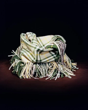 Close-up studio shot of a neatly folded fringed scarf featuring a plaid pattern of white, green, and yellow hues.