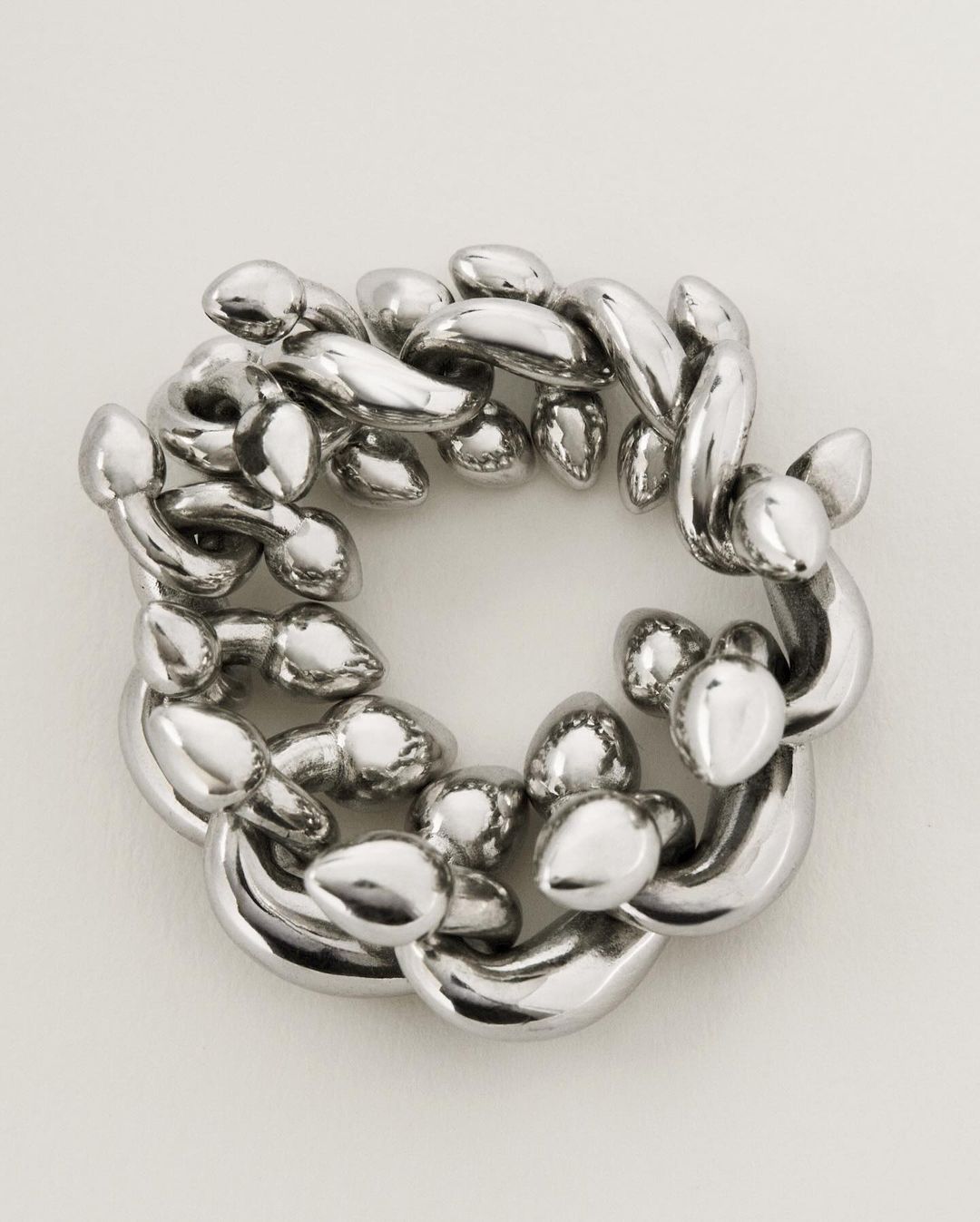 Abstract looping silver chain sculpture on a neutral backdrop with smooth textures, reflective surfaces, and an intricate circular arrangement.