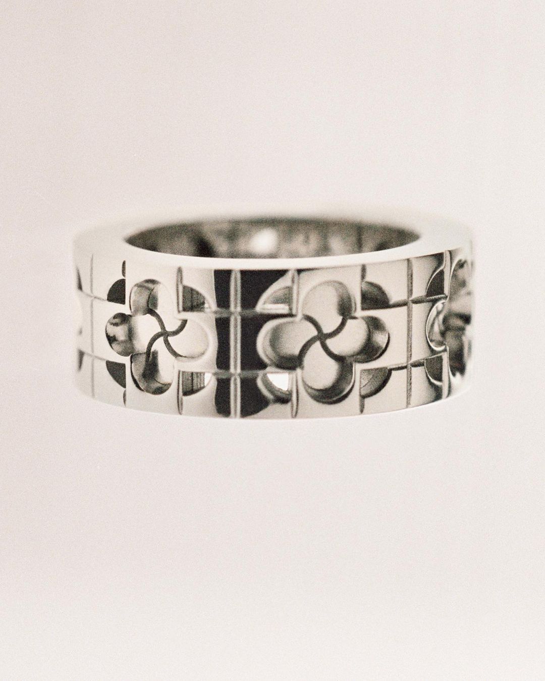 Close-up of a silver metal ring featuring cut-out geometric floral patterns against a pale white background. Jewelry for fashion.