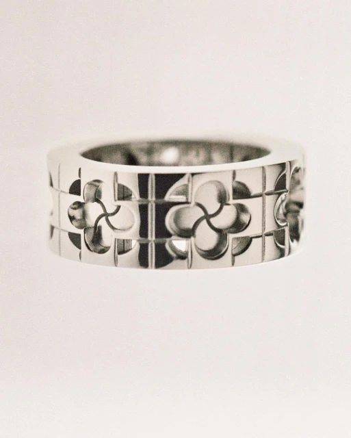 Close-up of a silver metal ring featuring cut-out geometric floral patterns against a pale white background. Jewelry for fashion.