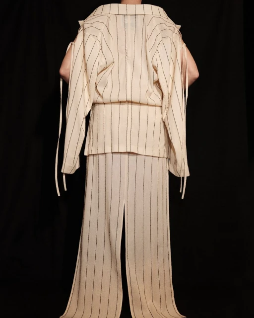 Back view of a person in a cream-colored, vertically striped matching set, including a jacket and pants, against a black backdrop.