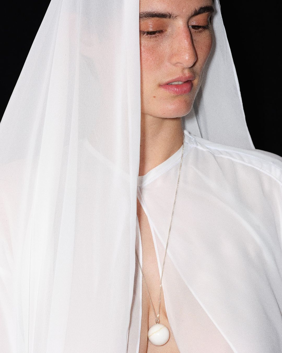 Close-up of a person draped in white fabric, showcasing fashion and beauty with a minimalist aesthetic against a dark backdrop.