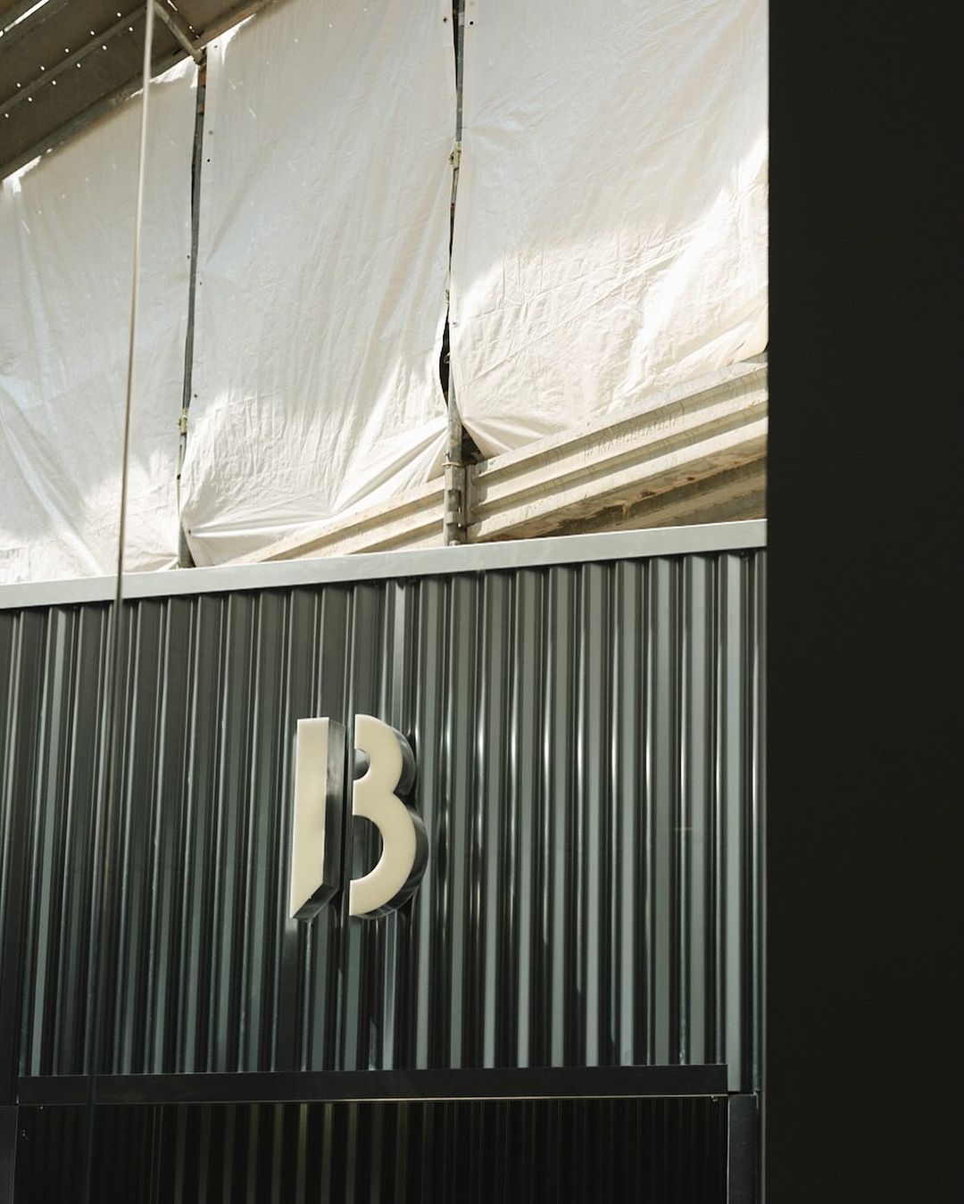 Silver number 13 on a corrugated metal surface with a white tarp overhead, creating an industrial, textured composition.