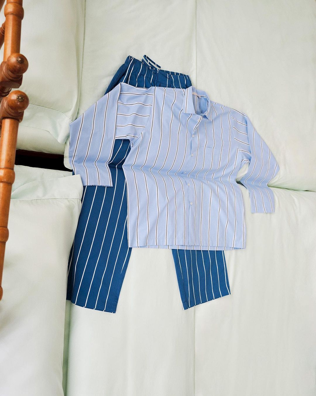 Striped pajama set on a white bed. Blue and white striped pants are paired with a light blue button-down pajama top.