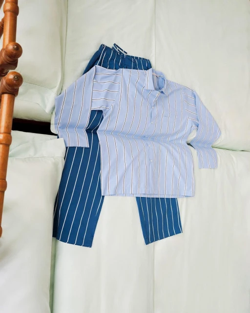 Striped pajama set on a white bed. Blue and white striped pants are paired with a light blue button-down pajama top.