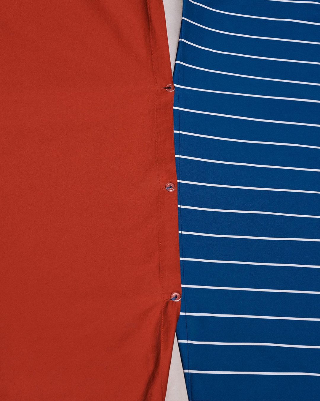 Close-up of two fabrics: a solid orange fabric with button accents next to a blue and white striped fabric.