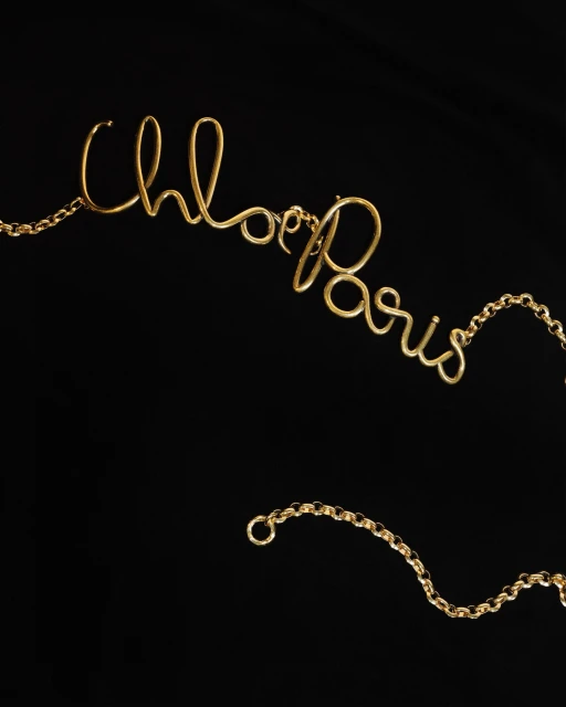 Gold necklace spelling 'Chloe Paris' on a black background, showcasing jewelry design and craftsmanship.