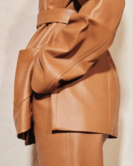 Close-up shot of a tan leather belted coat featuring a pocket, showcasing fashion design, material texture, and neutral color tones.