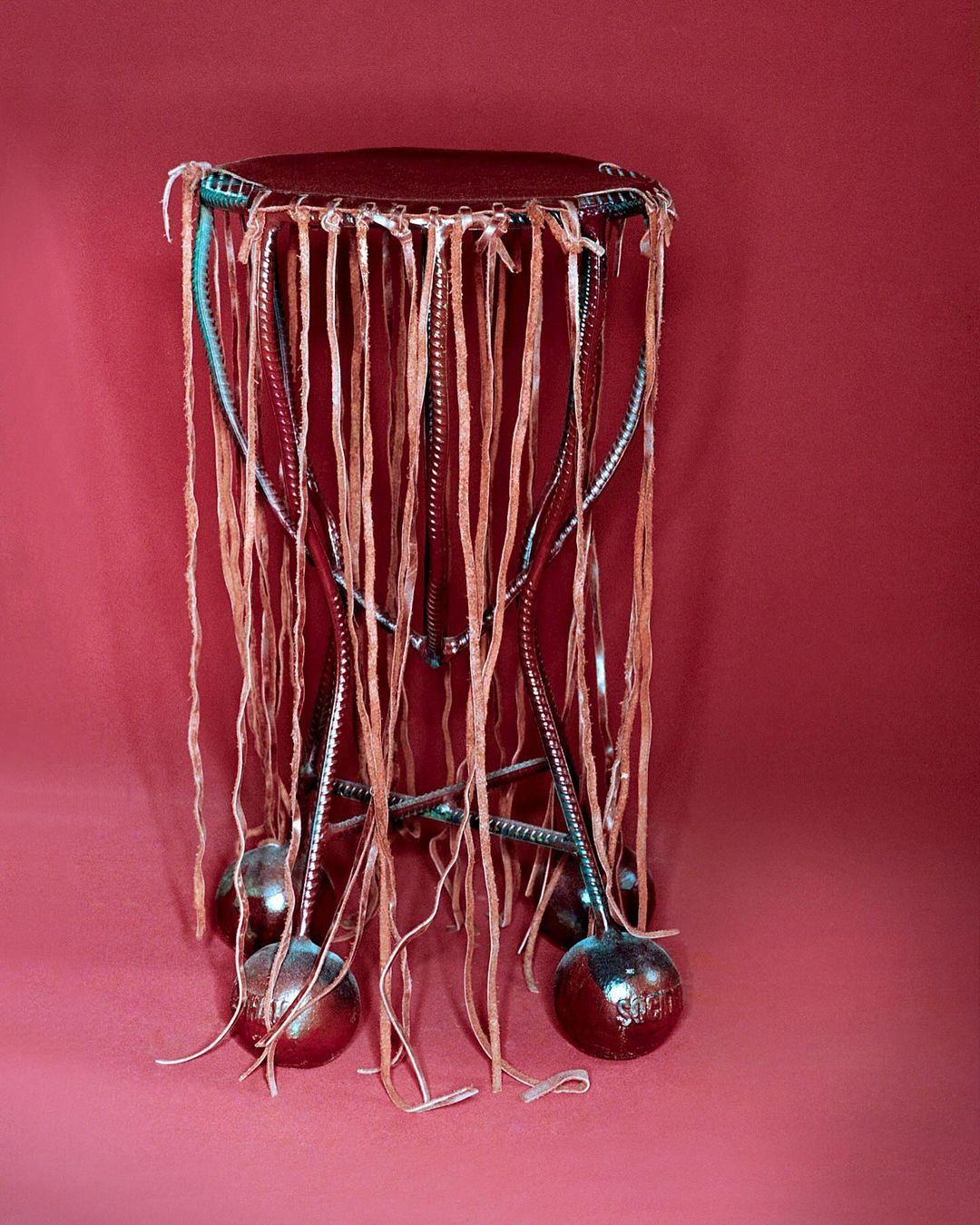 Studio shot of a drum-like percussion instrument featuring a dark wood top, metal frame, and hanging beige and silver ribbon details.