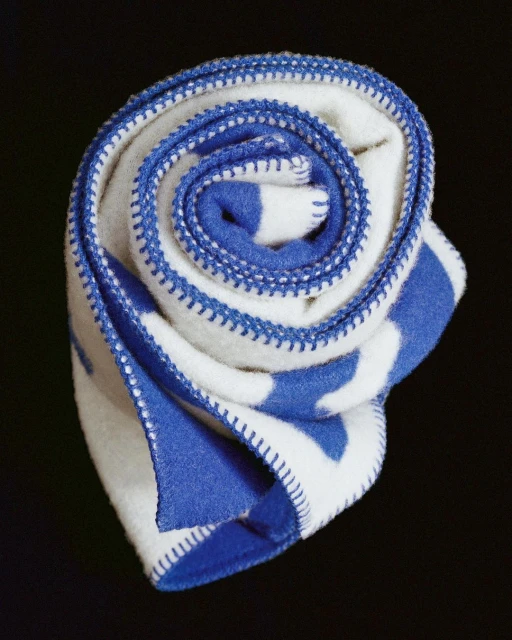 Close-up of a rolled, soft white blanket with blue stripes and blue overcast stitching edges, set against a dark backdrop.