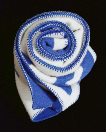 Close-up of a rolled, soft white blanket with blue stripes and blue overcast stitching edges, set against a dark backdrop.