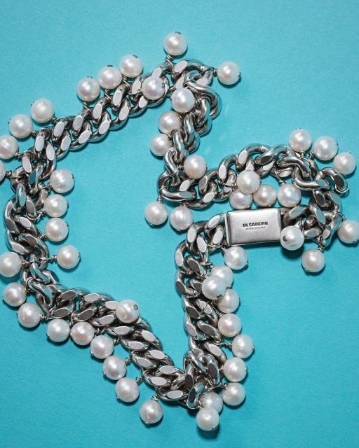 Close-up of a chunky silver chain necklace adorned with white pearl embellishments, set against a vibrant aqua blue background.