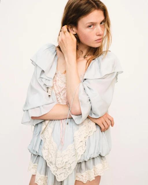 Woman with long brown hair in light blue dress with lace trim posing in a studio. Fashion shot with a neutral backdrop and soft lighting.