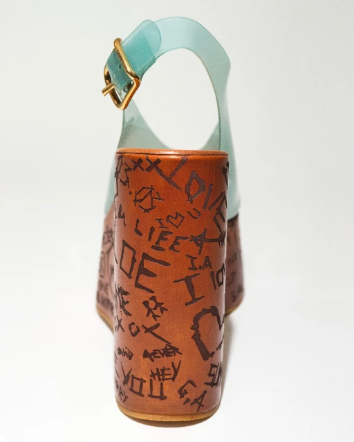 High-heeled platform sandal with a chunky heel, woodgrain finish, black writing, and clear blue upper strap, on a white background.