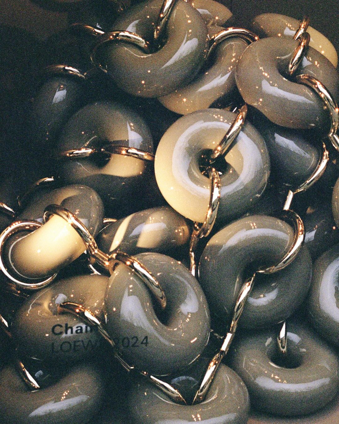 Pile of olive-green, donut-shaped pendants linked by gold hardware, with a partial logo visible on one of the pendants.