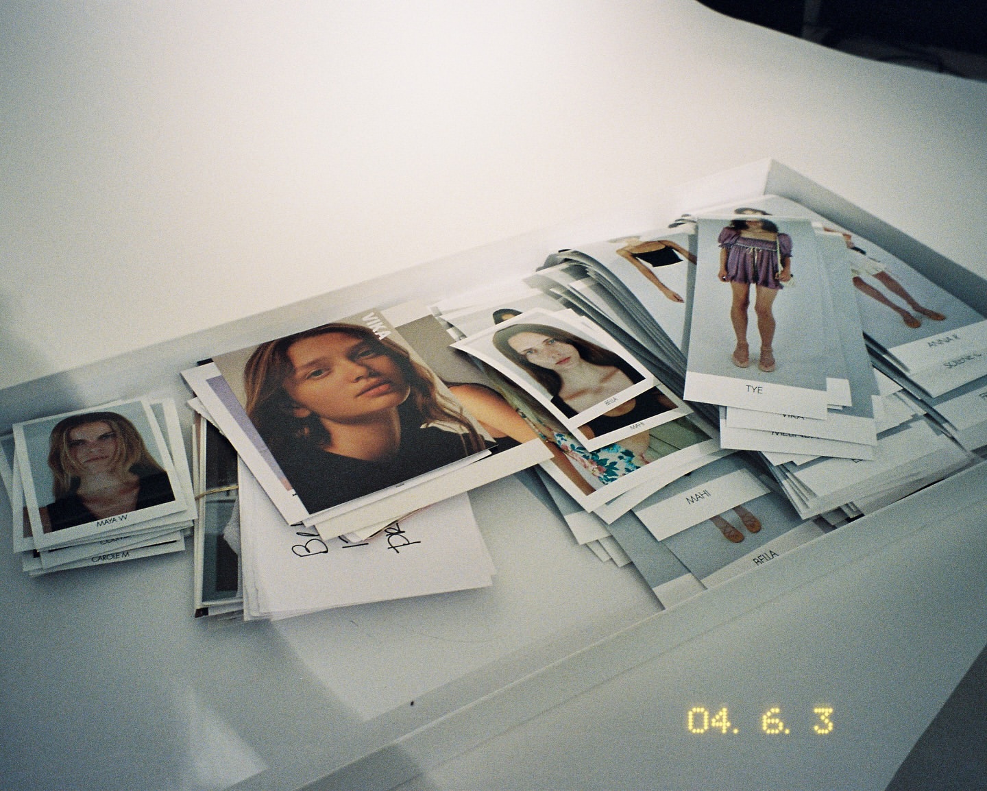 Model Polaroids are arranged in a tray; several young adult females are featured in the photos. The polaroids appear to be casting photos.