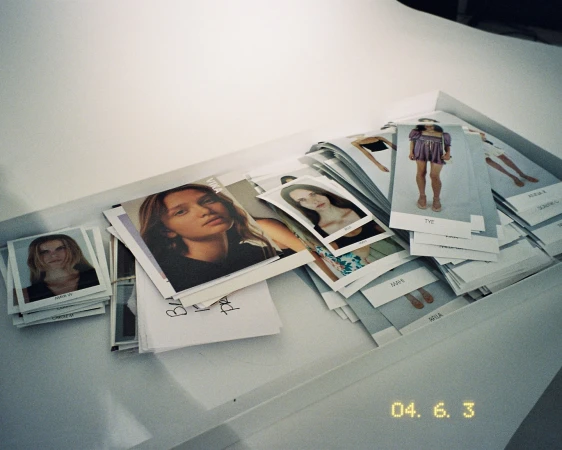 Model Polaroids are arranged in a tray; several young adult females are featured in the photos. The polaroids appear to be casting photos.