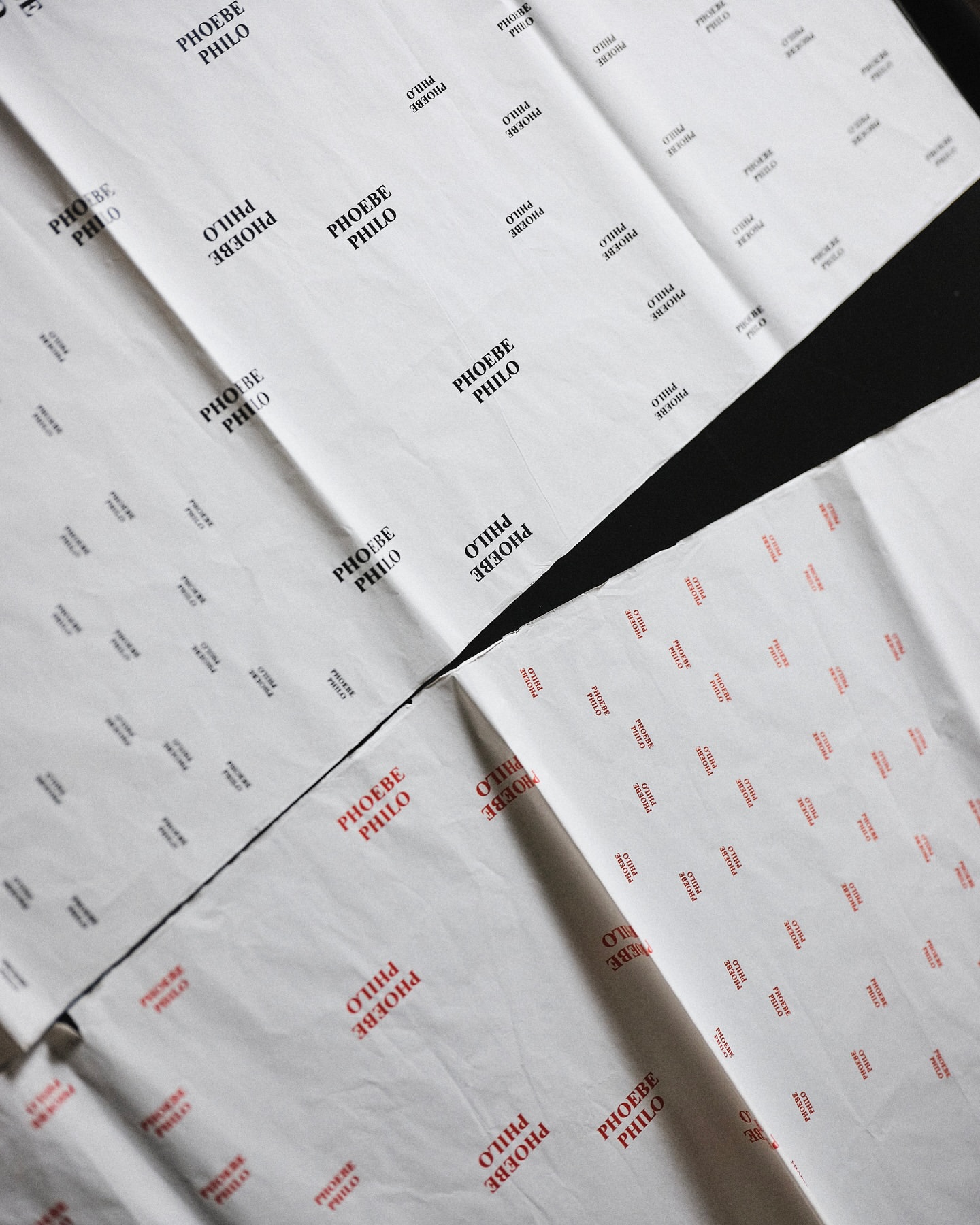 Sheets of white tissue paper featuring black and red repeating patterns of the fashion designer's name, 'Phoebe Philo,' laid flat.