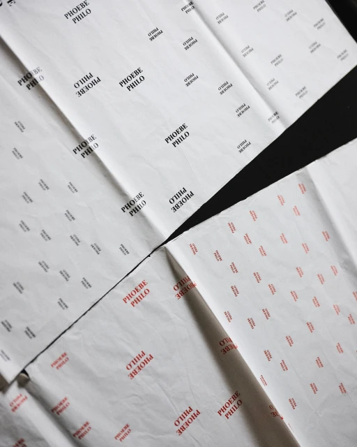 Sheets of white tissue paper featuring black and red repeating patterns of the fashion designer's name, 'Phoebe Philo,' laid flat.
