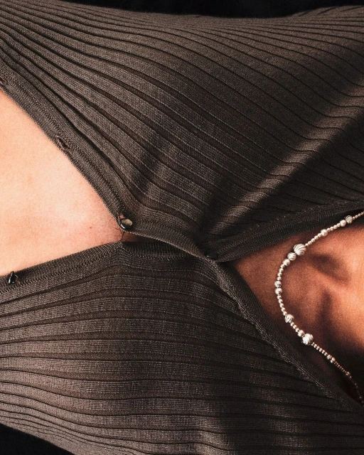 Woman wearing a brown, ribbed, button-down shirt with a silver beaded necklace, showcasing fashion and style in a close-up indoor shot.