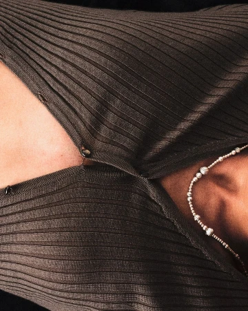 Woman wearing a brown, ribbed, button-down shirt with a silver beaded necklace, showcasing fashion and style in a close-up indoor shot.