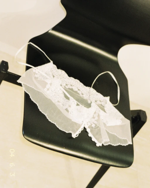 Lace lingerie top on a black chair. Intimate apparel detail shot. Wedding or boudoir fashion. Soft light, pale tones, close up.
