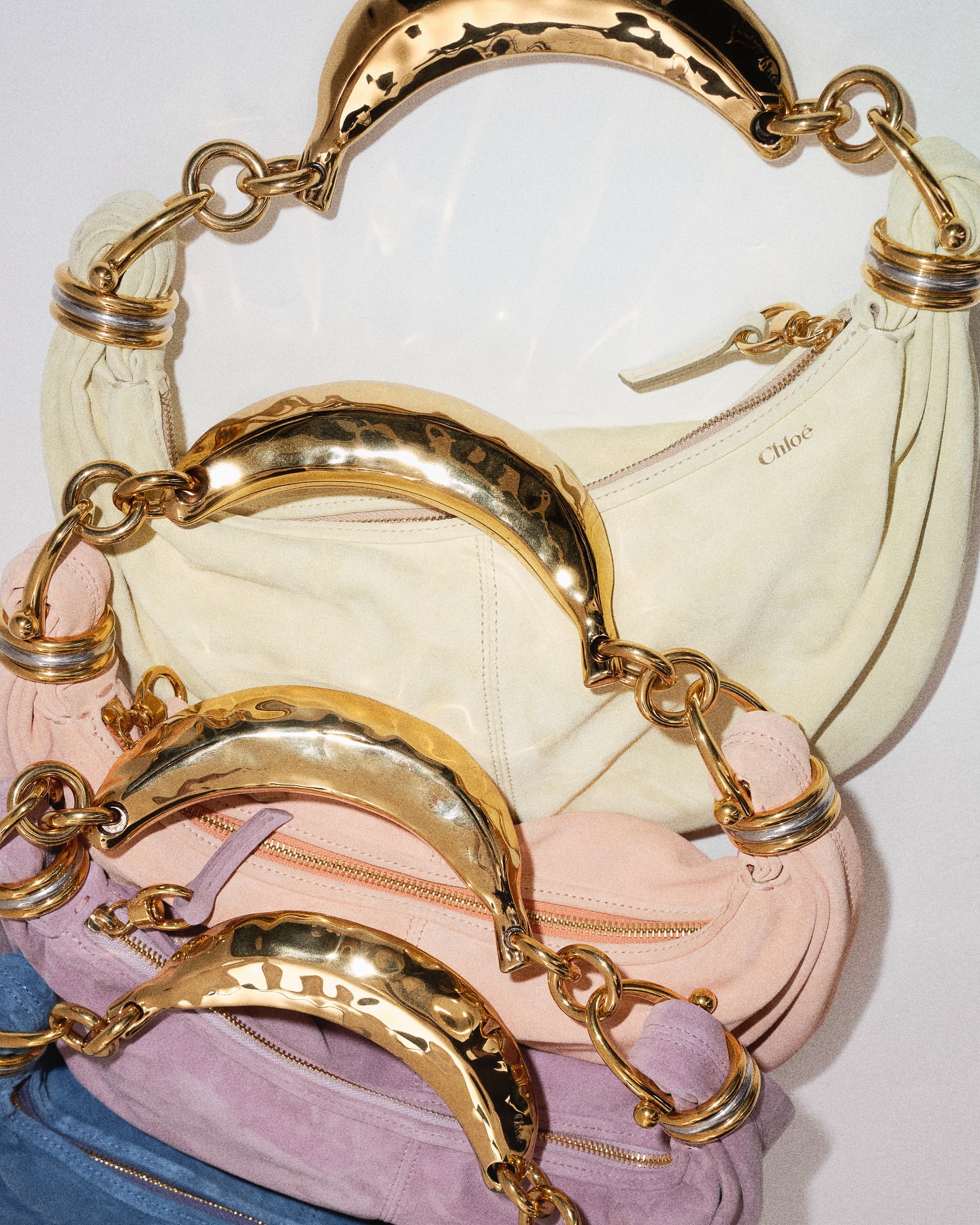 Stack of Chloe handbags with gold chain handles in various pastel colors against a white background in a fashion editorial shot.