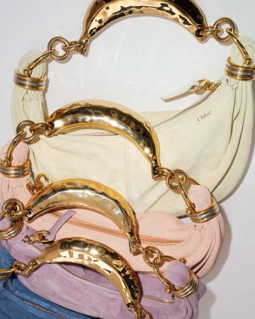 Stack of Chloe handbags with gold chain handles in various pastel colors against a white background in a fashion editorial shot.