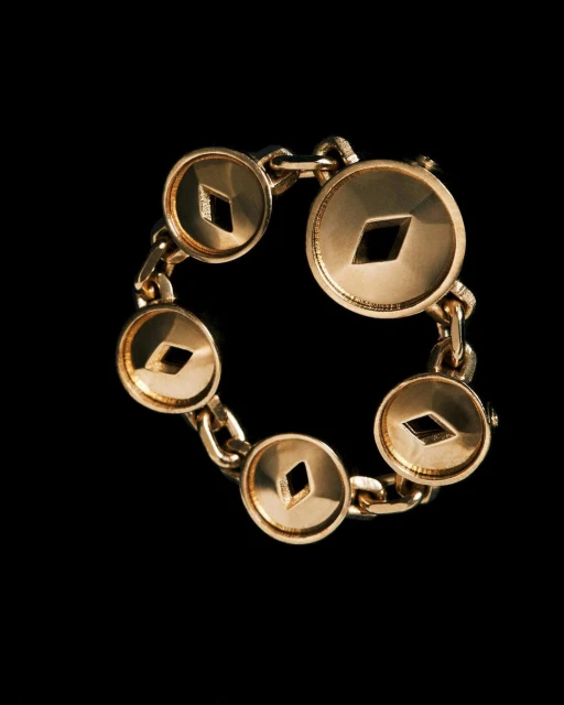 Gold metal bracelet with round charms and diamond-shaped cutouts on a dark background, jewelry design, fashion accessory.