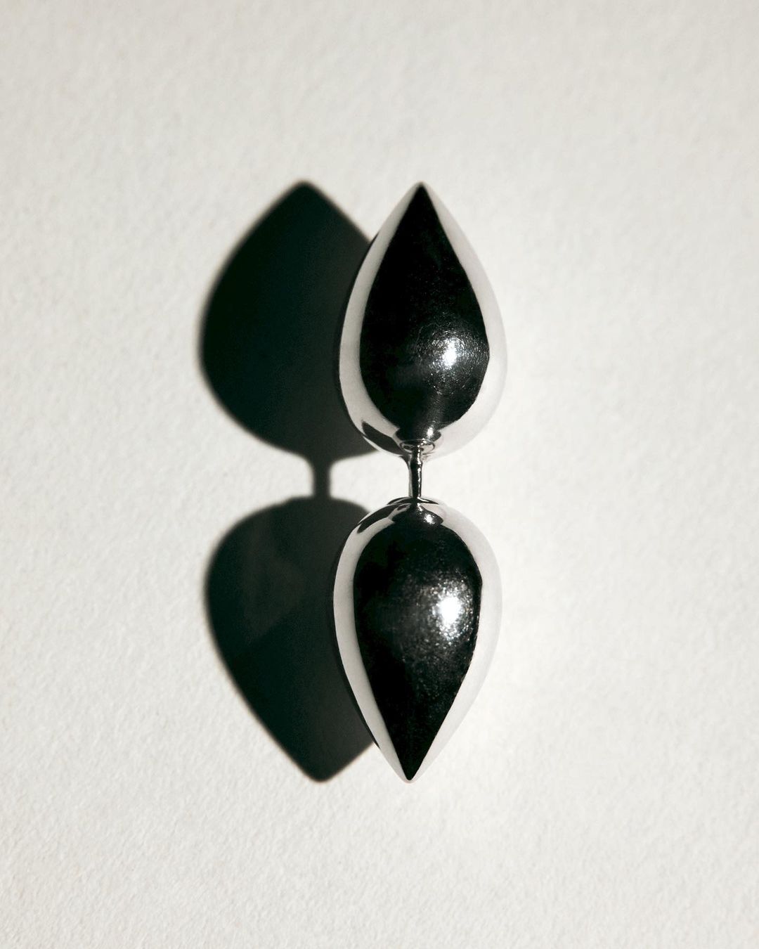 Studio shot of a silver metallic sculpture featuring two teardrop shapes stacked vertically against a plain white backdrop with a shadow.