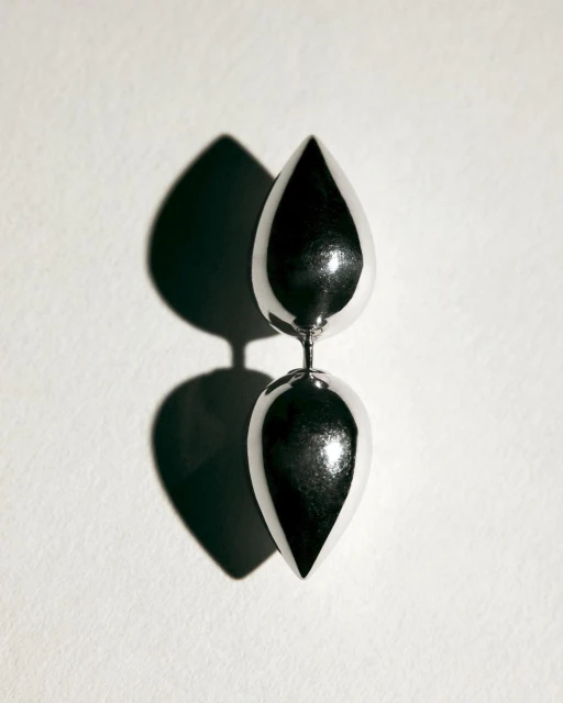 Studio shot of a silver metallic sculpture featuring two teardrop shapes stacked vertically against a plain white backdrop with a shadow.