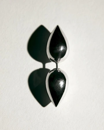 Studio shot of a silver metallic sculpture featuring two teardrop shapes stacked vertically against a plain white backdrop with a shadow.