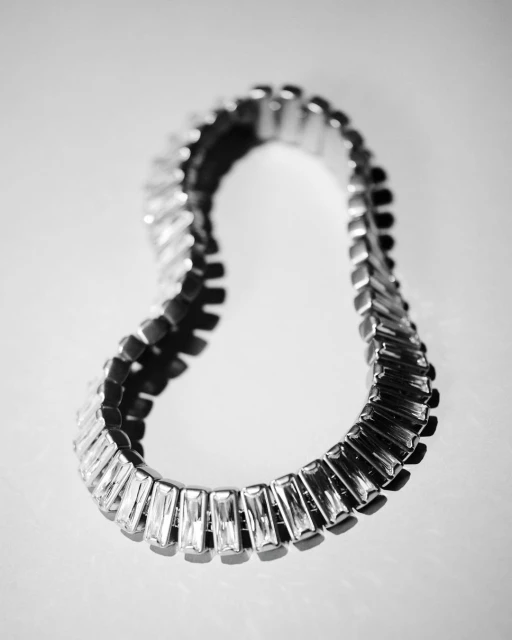 Close-up studio shot of a silver-toned metal stretch bracelet with clear baguette-cut stones against a bright reflective surface.