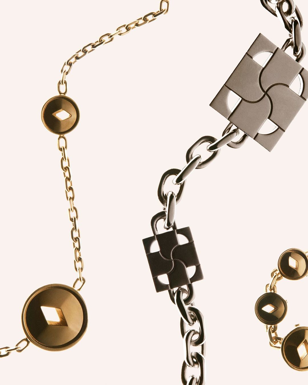 Close-up of a gold and silver metal chain necklace with geometric square and circular details against a neutral background in a studio setting.
