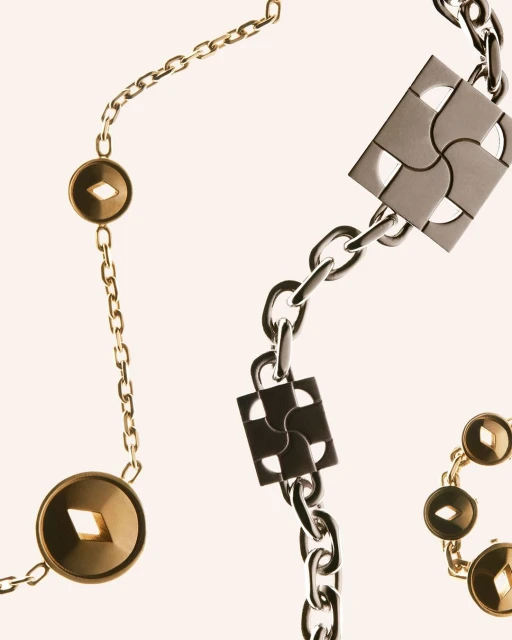 Close-up of a gold and silver metal chain necklace with geometric square and circular details against a neutral background in a studio setting.