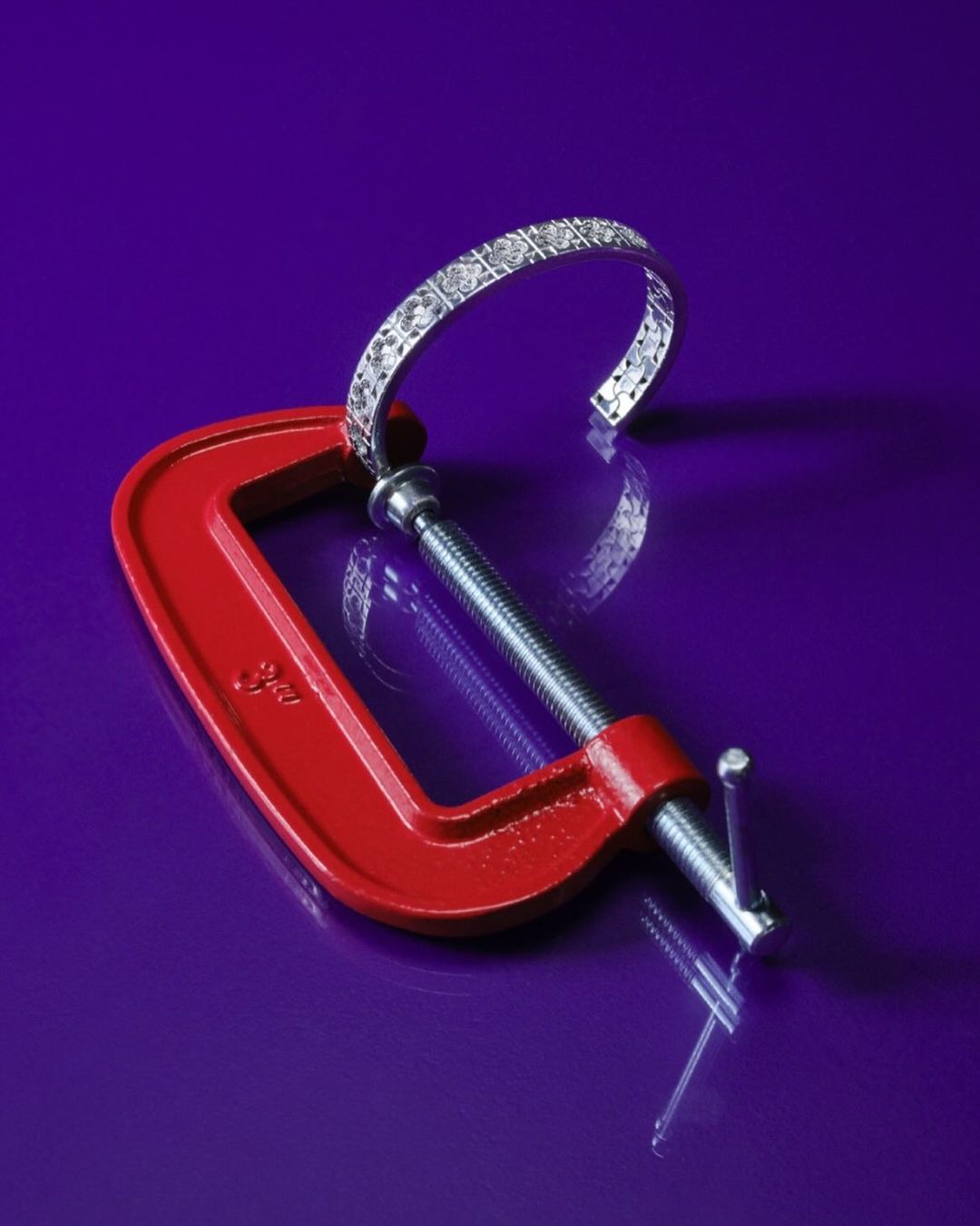 Open diamond bracelet is held in place by a red metal clamp against a purple background, highlighting jewelry design and functionality.