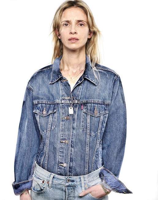 Woman in denim jacket and jeans in a studio shot. She is fair-skinned with blonde hair, wearing simple jewelry and casual attire.