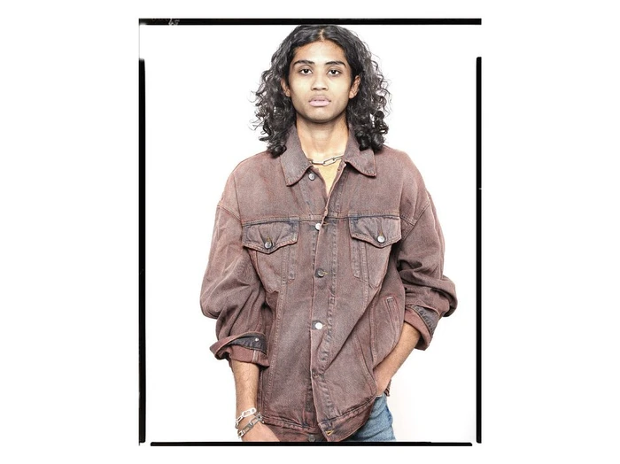Portrait of a man with long curly dark hair wearing a brown denim jacket against a white background by Ilario Magali