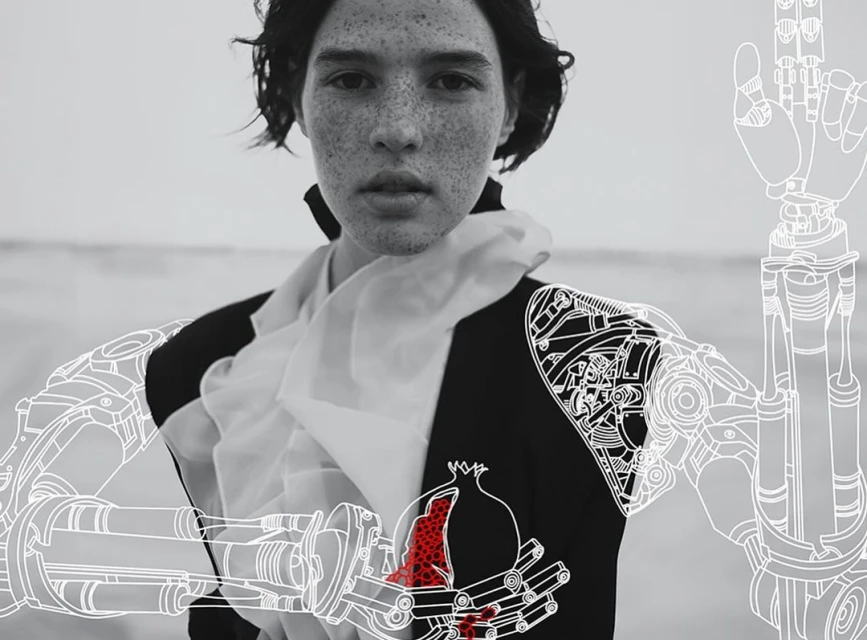 Artistic black and white portrait of person with freckles wearing dark jacket with mechanical arm line art and red pomegranate.