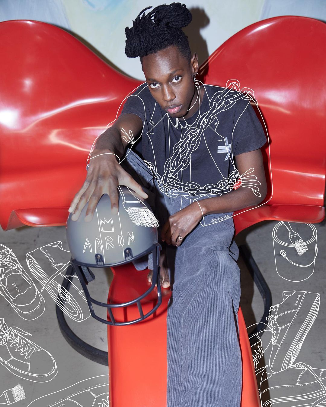 Young adult with braided hair poses with a helmet while sitting on a red chair with line drawing effect on the background.